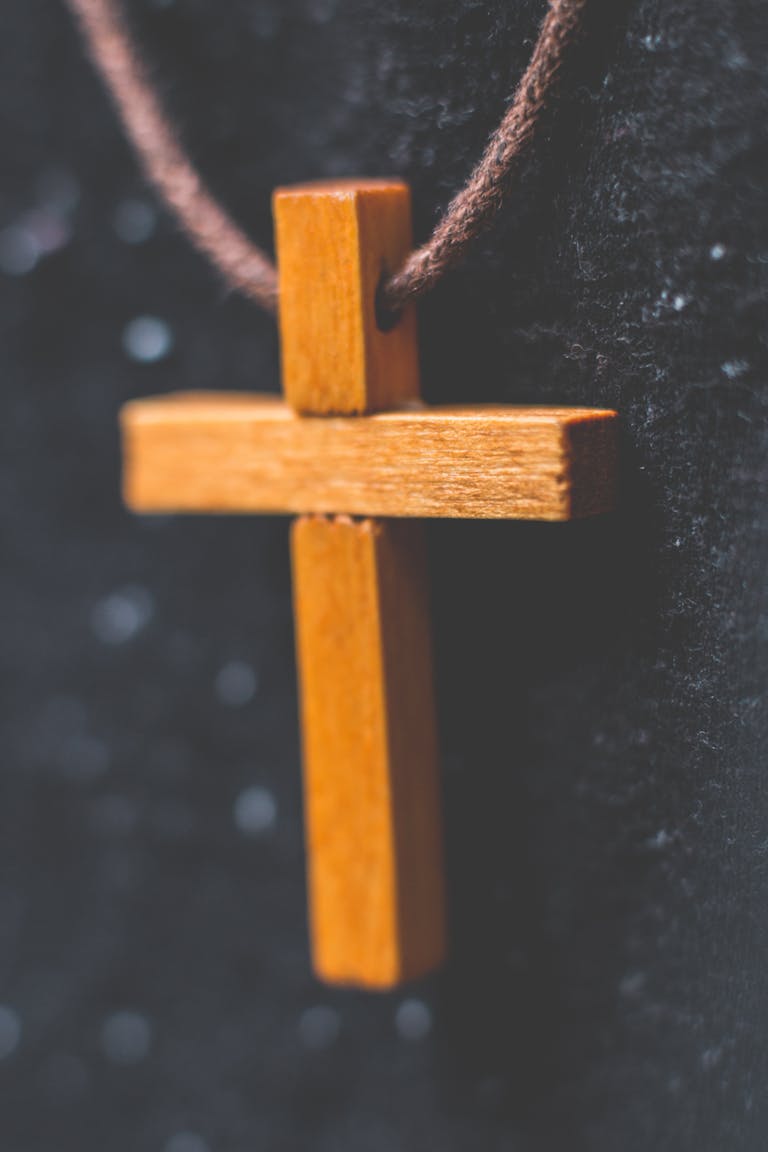 Detailed close-up of a hanging wooden cross necklace on a fabric background.